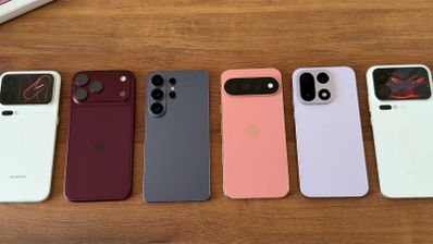 Seis smartphones de diferentes marcas y colores colocados en fila sobre una superficie de madera, mostrando sus módulos de cámara traseros.