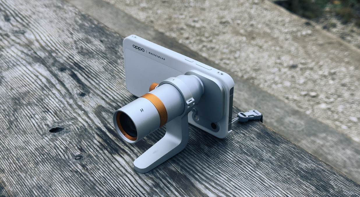 Objetivo externo con anillo naranja acoplado a la parte trasera de un OPPO Find X10 Pro Max sobre una superficie de madera.