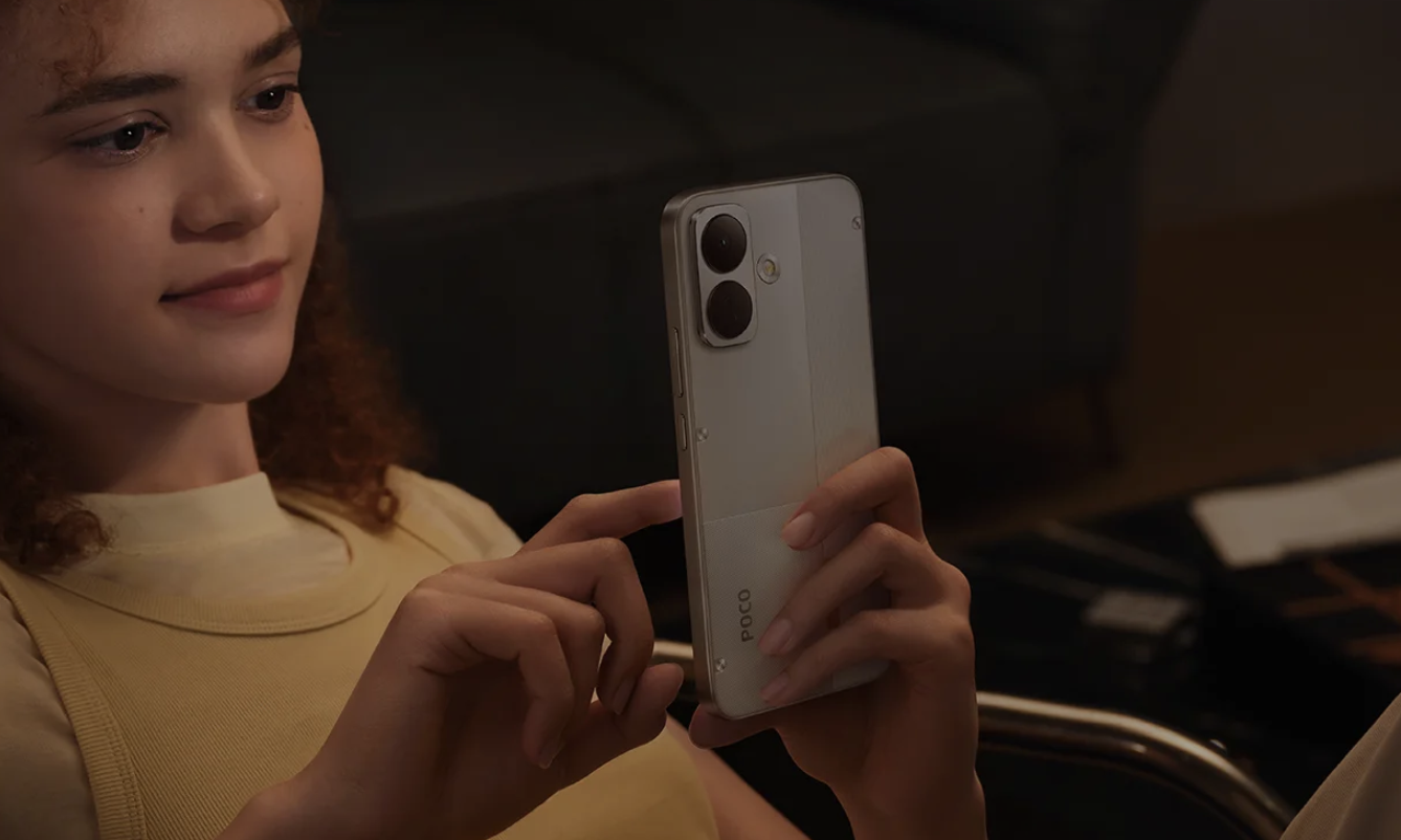 Mujer joven interactuando con la pantalla de un teléfono POCO X8 en color blanco en un entorno interior.