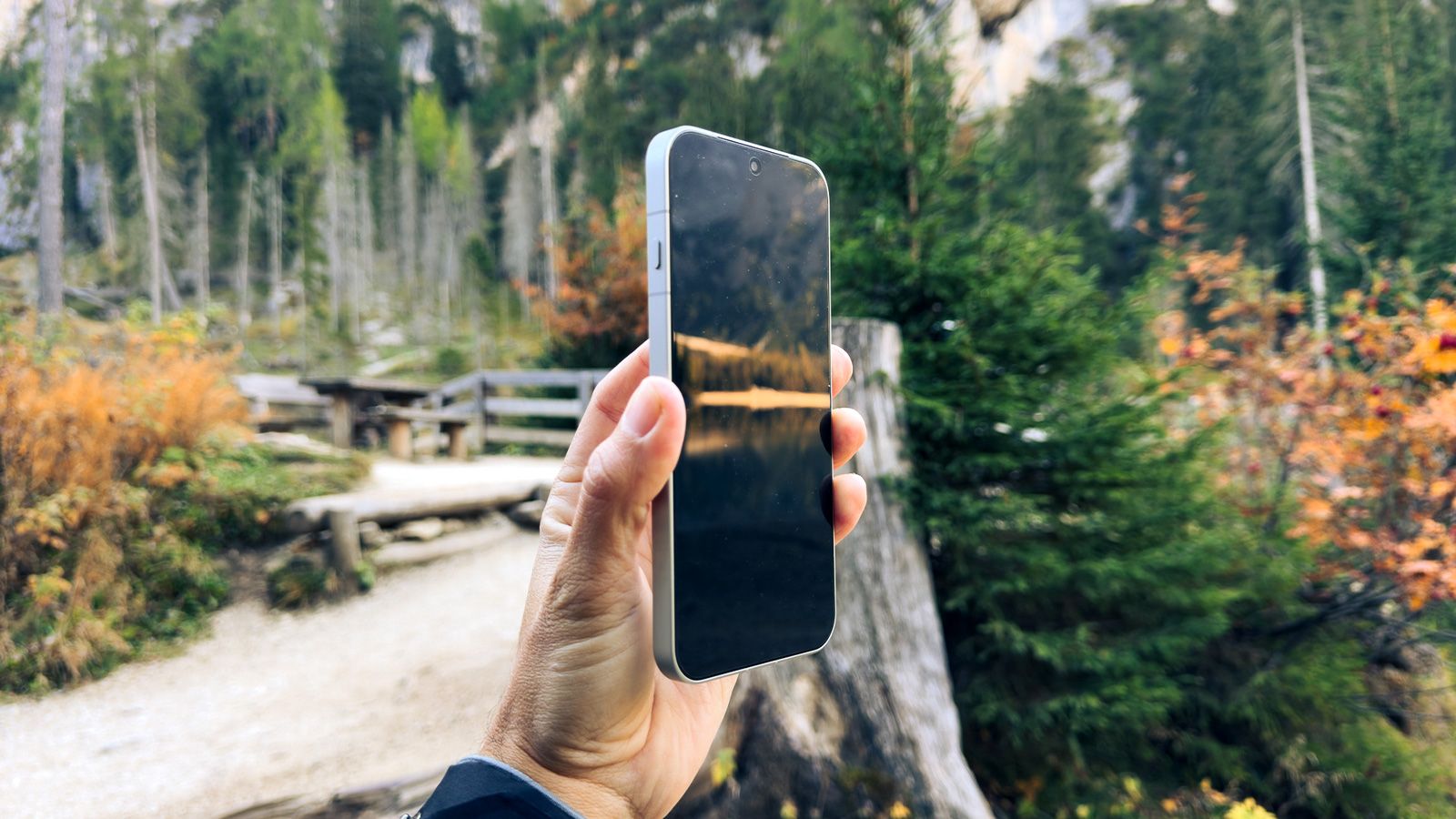 Mano sujetando un OPPO Find X10 Pro Max de perfil en un entorno natural con árboles y vegetación otoñal.