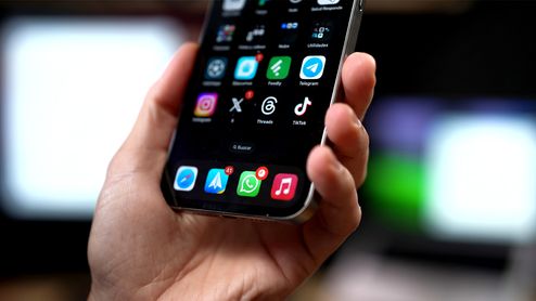 Mano sujetando un iPhone con la aplicación de WhatsApp visible en el dock inferior y notificaciones pendientes.