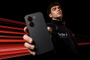 Parte trasera del teléfono móvil Redmi Turbo 5 sostenido por un hombre con fondo de estelas de luz rojas.