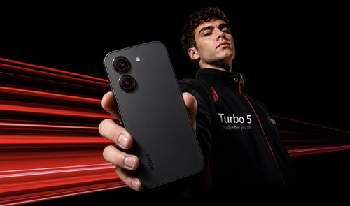 Parte trasera del teléfono móvil Redmi Turbo 5 sostenido por un hombre con fondo de estelas de luz rojas.