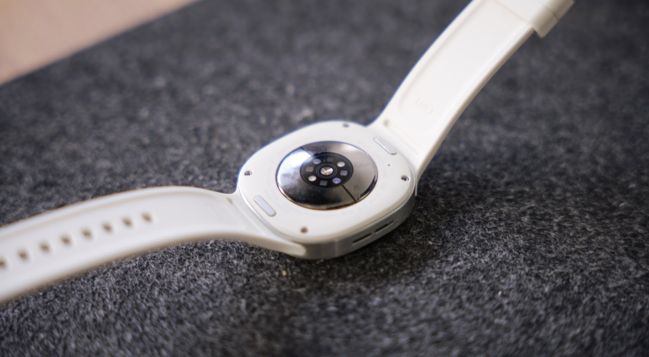 Parte posterior de un Samsung Galaxy Watch9 con correa blanca mostrando los sensores biométricos y de salud.