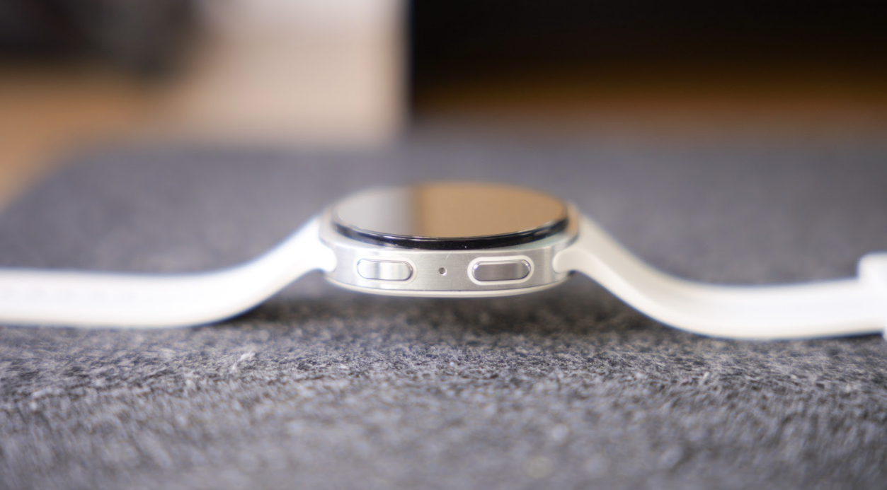 Plano lateral del Samsung Galaxy Watch9 mostrando los dos botones físicos y el orificio del micrófono en el chasis plateado.