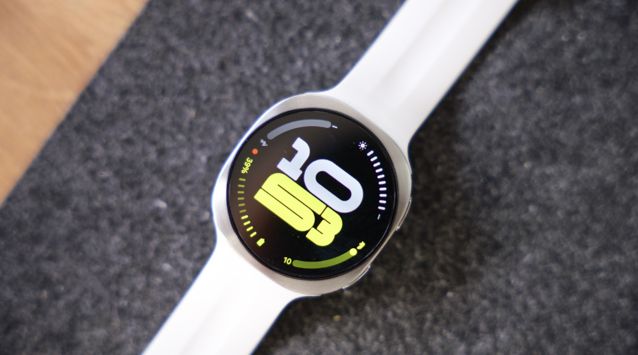Plano cenital del Samsung Galaxy Watch9 con correa blanca apoyado sobre una superficie gris de fieltro.