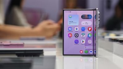 Smartphone plegable Samsung Galaxy Z-Fold8 apoyado verticalmente sobre una mesa blanca mostrando su pantalla principal con iconos de aplicaciones y widgets.