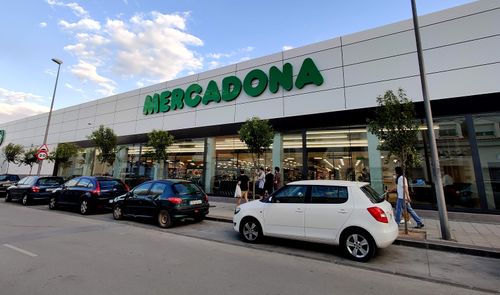 Fachada exterior de un supermercado Mercadona con clientes y vehículos aparcados