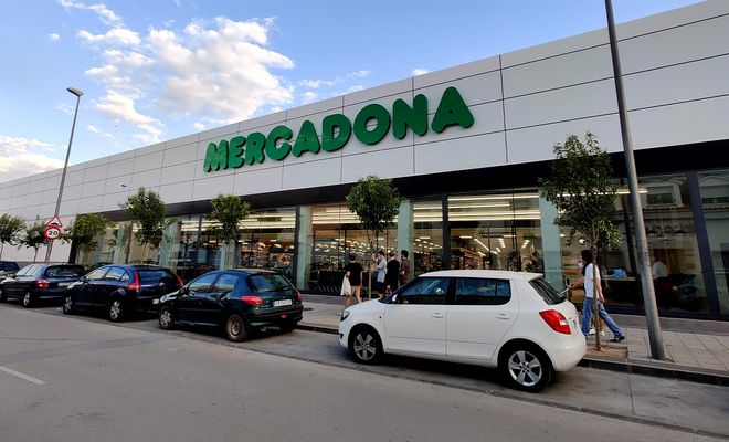 Fachada exterior de un supermercado Mercadona con clientes y vehículos aparcados