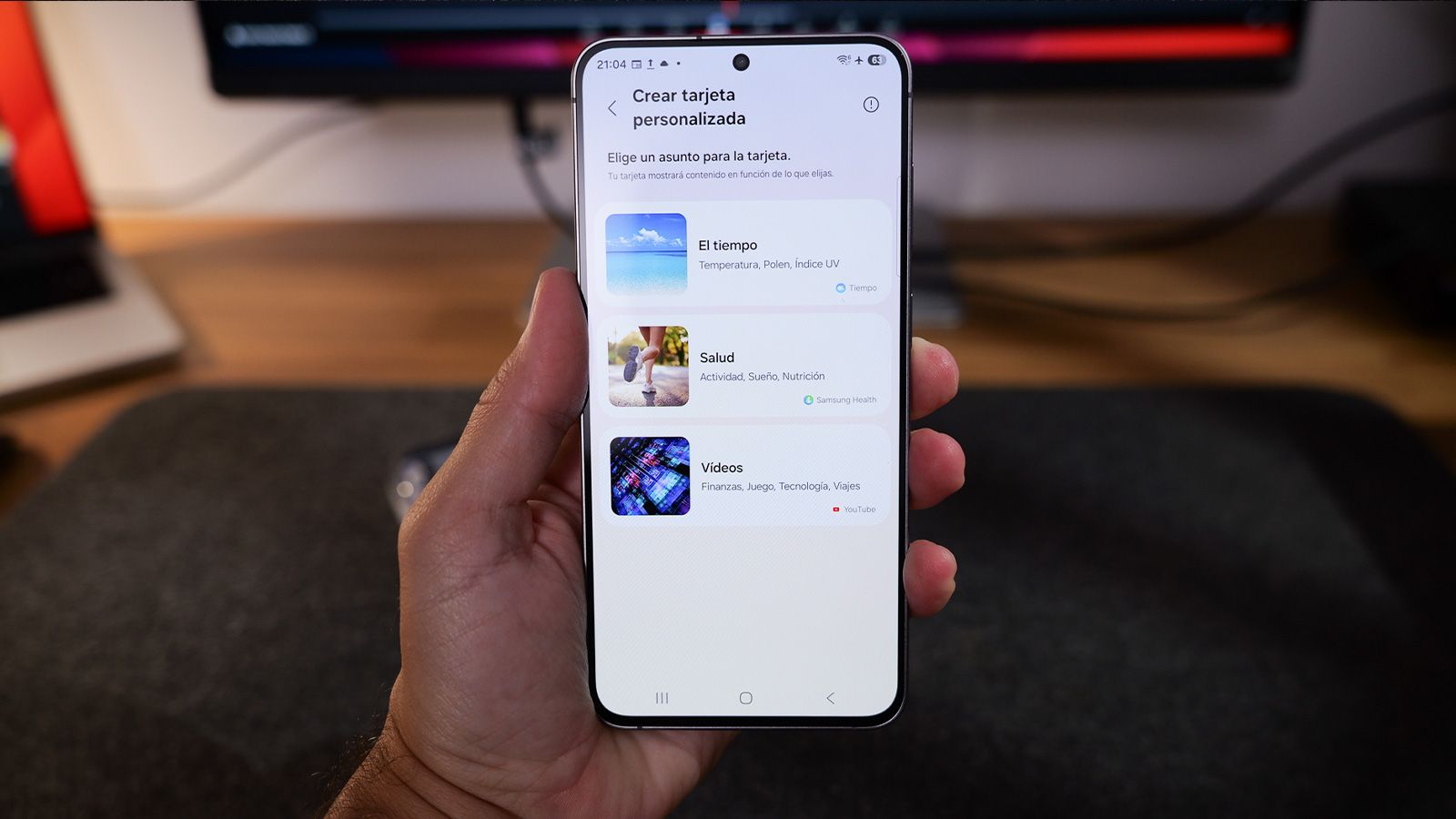 Primer plano de una mano sujetando un teléfono Samsung con el menú de creación de tarjetas personalizadas de One UI 9 abierto.