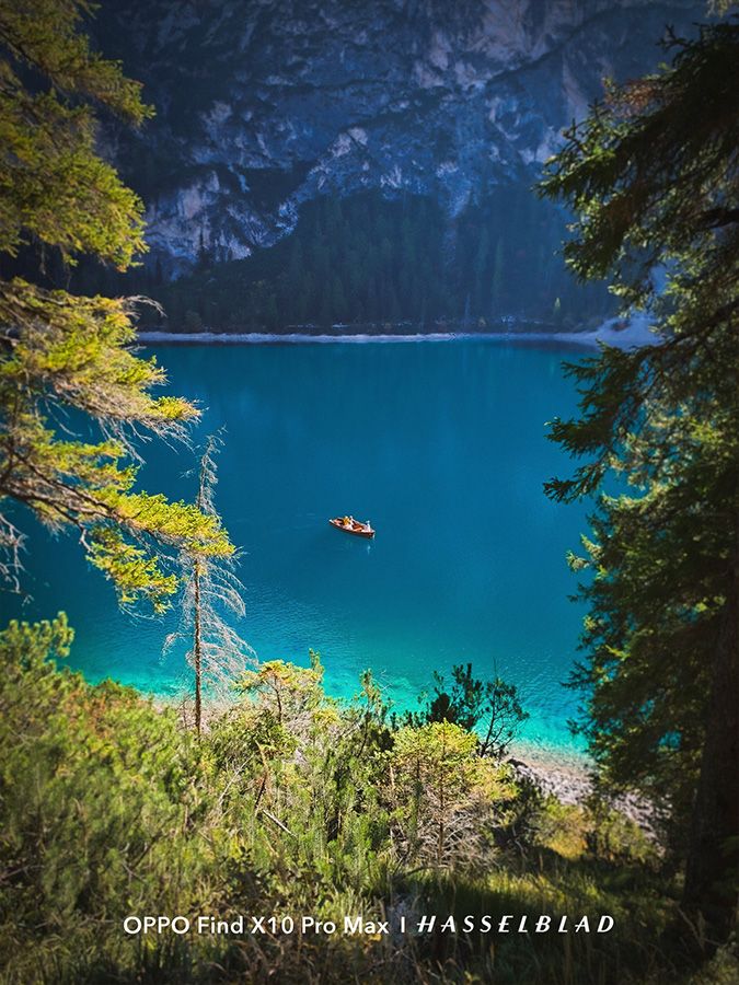 Plano general de un lago de aguas turquesas entre montañas y árboles con una pequeña barca en el centro.