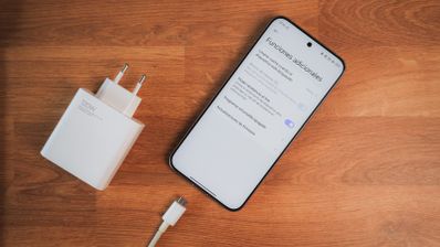Teléfono móvil Xiaomi 15T Pro con la pantalla encendida junto a su cargador de pared y cable USB sobre una superficie de madera.