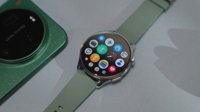 Reloj inteligente Xiaomi Watch 5 con pantalla circular y correa verde junto a un teléfono móvil con módulo de cámara Leica.