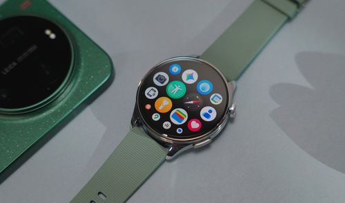 Reloj inteligente Xiaomi Watch 5 con pantalla circular y correa verde junto a un teléfono móvil con módulo de cámara Leica.