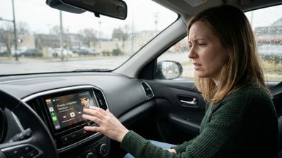 Mujer con expresión de confusión interactuando con la pantalla táctil de un coche que muestra la interfaz de reproducción de música.