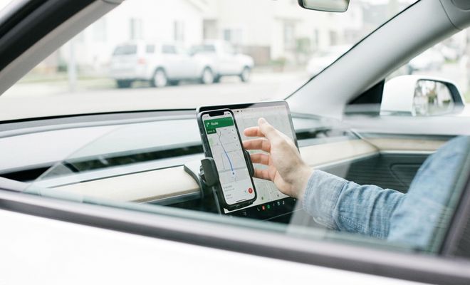 Conductor interactuando con la aplicación Google Maps en un smartphone colocado en el salpicadero de un coche.