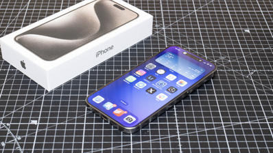 iPhone 15 Pro con la pantalla encendida junto a su caja sobre una base de corte cuadriculada.