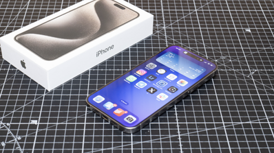 iPhone 15 Pro con la pantalla encendida junto a su caja sobre una base de corte cuadriculada.