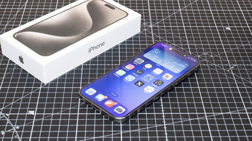 iPhone 15 Pro con la pantalla encendida junto a su caja sobre una base de corte cuadriculada.