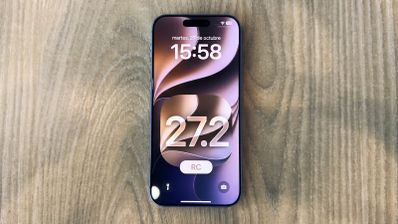Vista frontal de un iPhone 18 Pro mostrando la pantalla de bloqueo con el número 27.2 sobre una superficie de madera.
