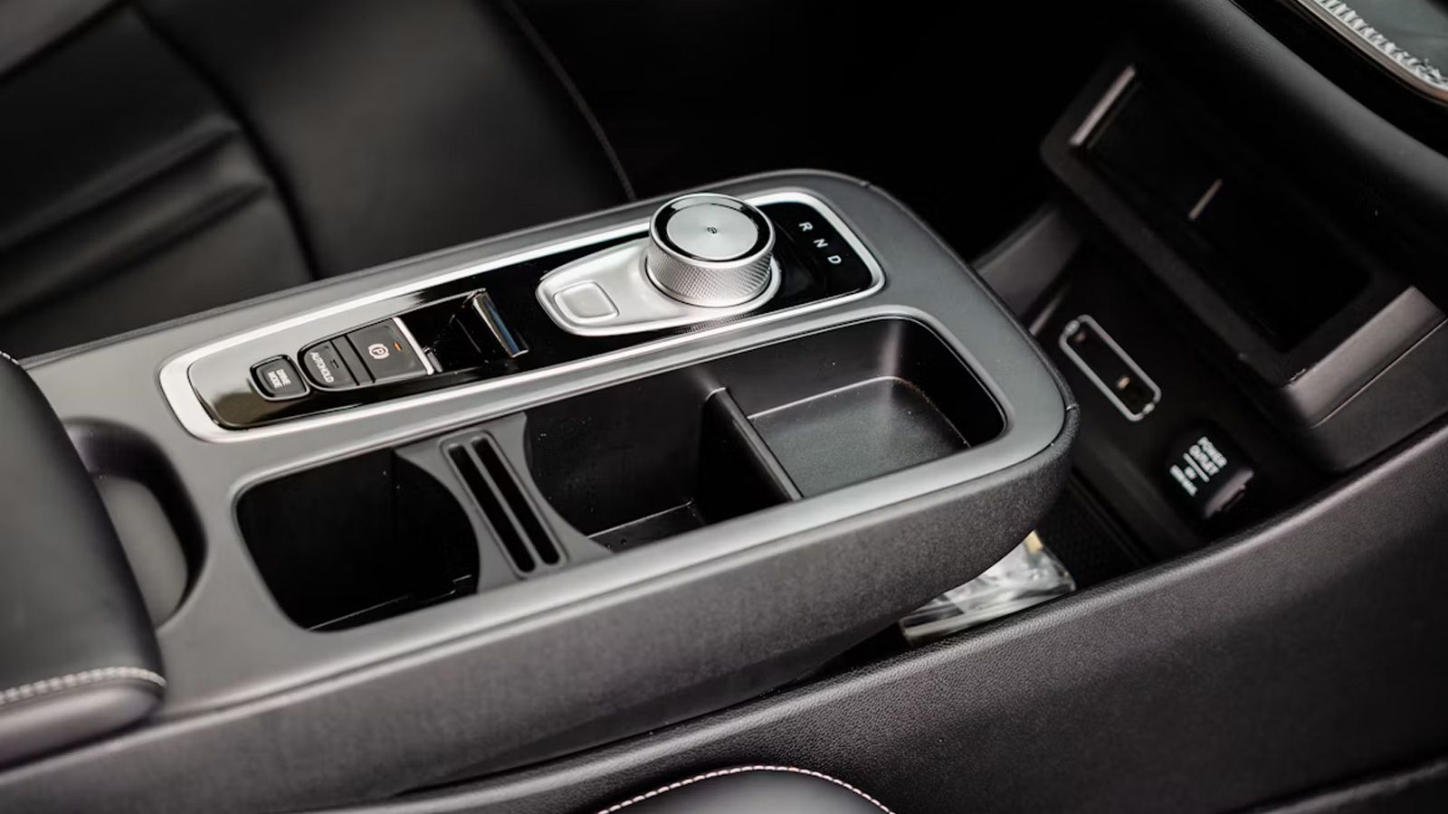 Consola central de un vehículo con selector de marchas rotativo y puertos de conexión USB.