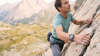Hombre escalando una pared de roca en la montaña con un reloj inteligente deportivo en su muñeca.