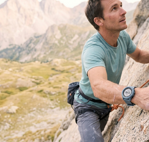 Hombre escalando una pared de roca en la montaña con un reloj inteligente deportivo en su muñeca.