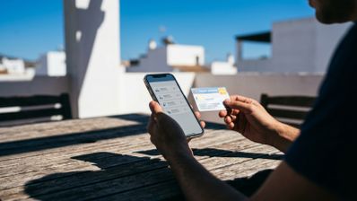 Persona consultando información sanitaria en un teléfono móvil mientras sostiene una tarjeta de salud.