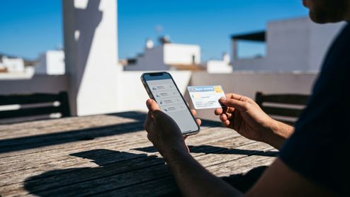 Persona consultando información sanitaria en un teléfono móvil mientras sostiene una tarjeta de salud.