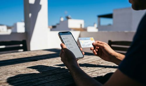 Persona consultando información sanitaria en un teléfono móvil mientras sostiene una tarjeta de salud.