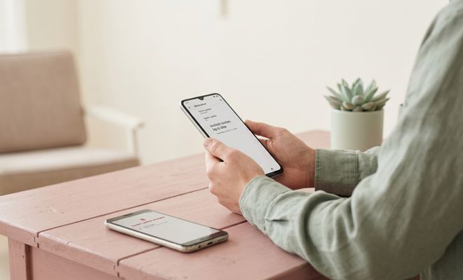 Persona sosteniendo un teléfono móvil con un mensaje de actualización de sistema en pantalla sentado frente a una mesa.