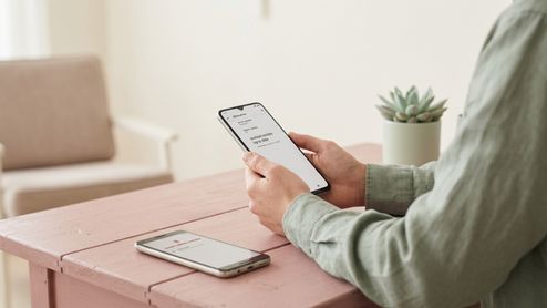 Persona sosteniendo un teléfono móvil con un mensaje de actualización de sistema en pantalla sentado frente a una mesa.
