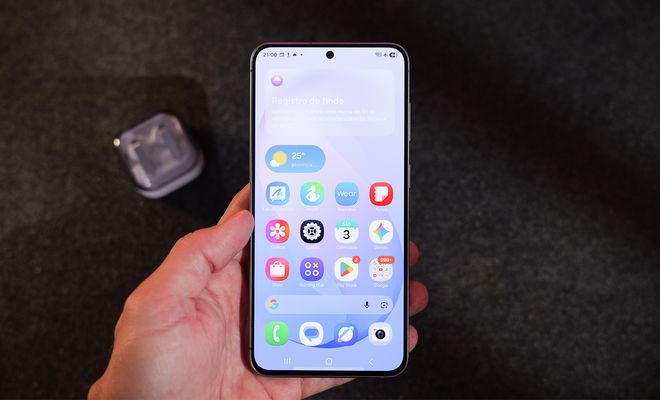 Mano sujetando un teléfono móvil Samsung con la pantalla de inicio de One UI 9 donde se aprecian iconos de aplicaciones y un widget meteorológico.