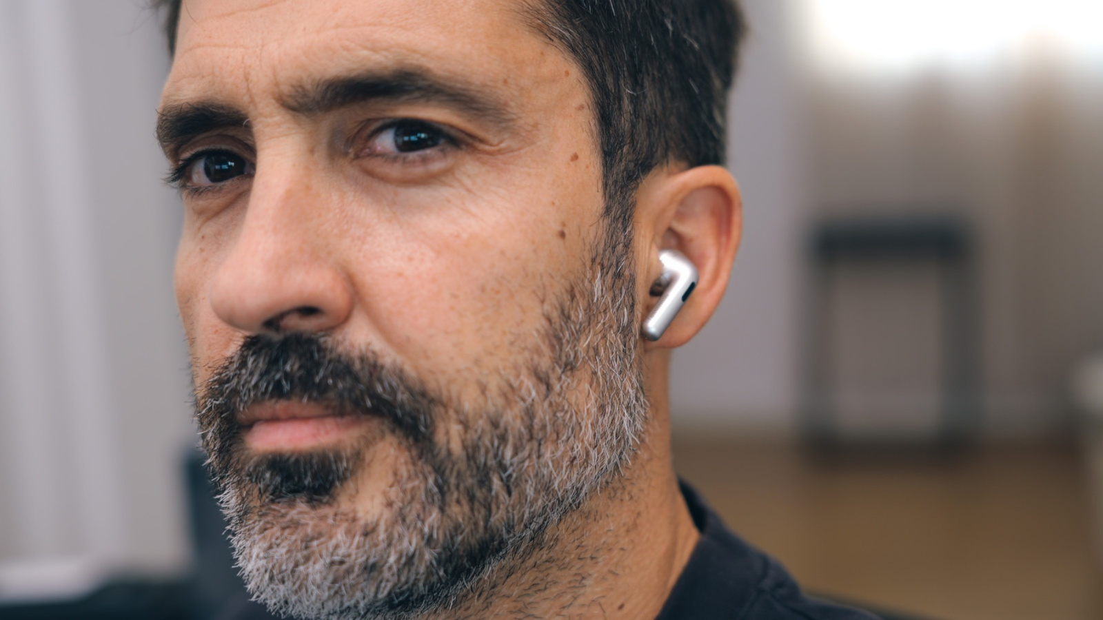 Hombre con barba de perfil luciendo un auricular inalámbrico OPPO Enco X4 de color plateado en su oreja izquierda.