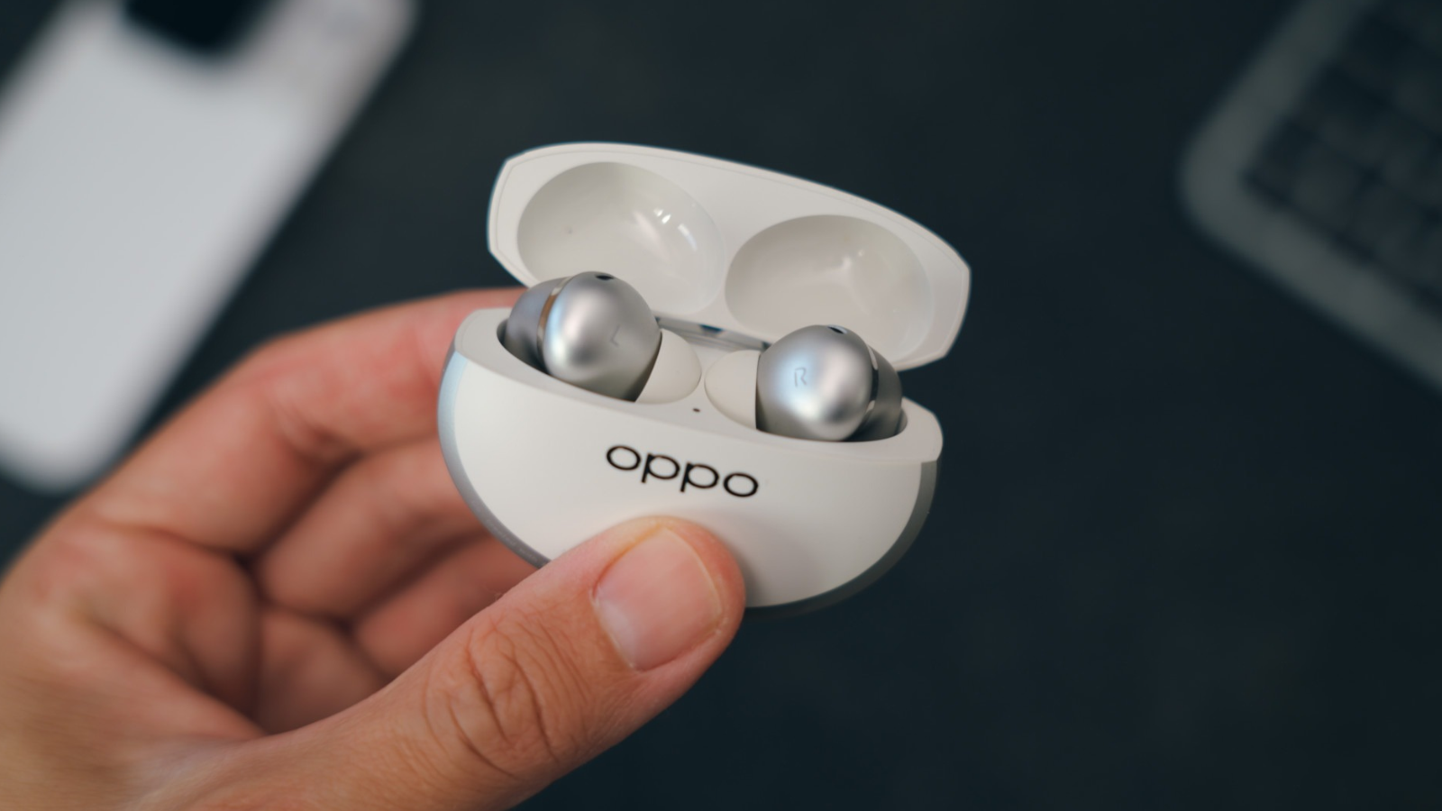 Mano sujetando el estuche de carga abierto con los auriculares OPPO Enco X4 en su interior.