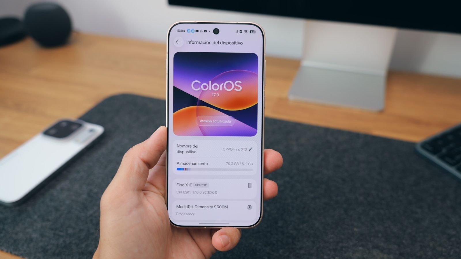 Primer plano de una mano sosteniendo un OPPO Find X10 mostrando el menú de ajustes con la versión de ColorOS 17 instalada.