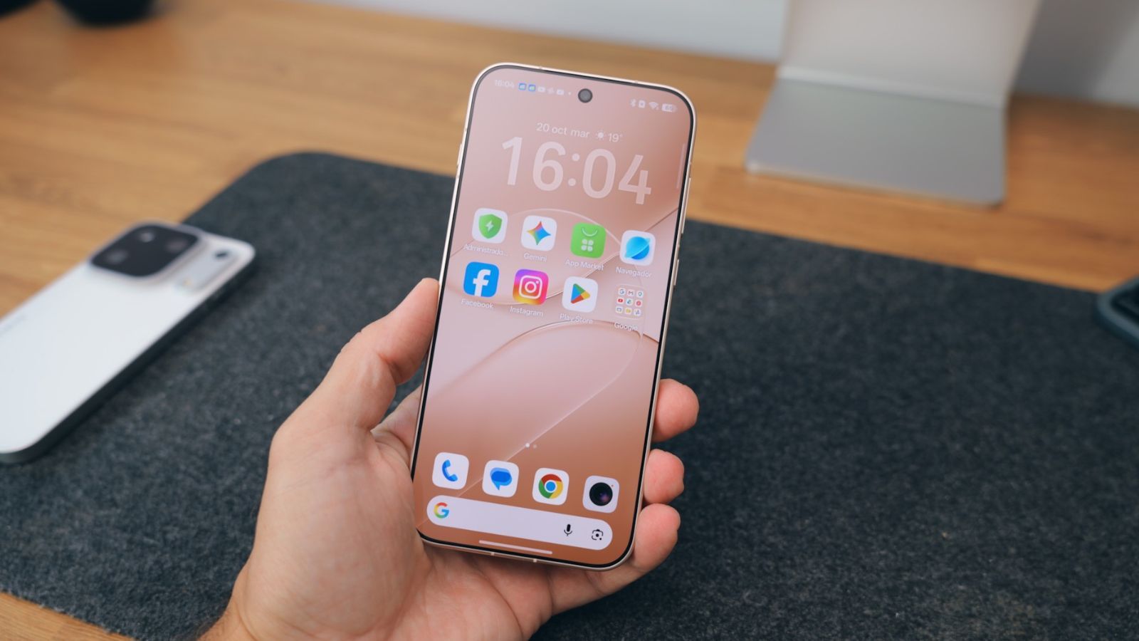 Primer plano de la pantalla de inicio de un OPPO Find X10 en la mano de un usuario sobre un escritorio.