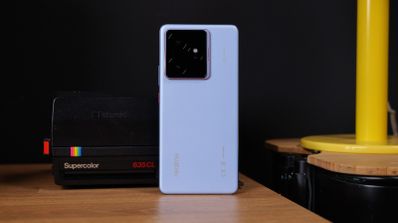 Parte trasera del teléfono móvil realme GT7 en color blanco con módulo de cámaras cuadrado situado junto a una cámara instantánea clásica.