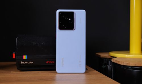 Parte trasera del teléfono móvil realme GT7 en color blanco con módulo de cámaras cuadrado situado junto a una cámara instantánea clásica.
