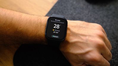 Smartwatch con pantalla rectangular en la muñeca mostrando la aplicación del tiempo con 28 grados.