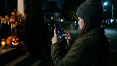 Persona ajustando la configuración de la cámara de su móvil para hacer una foto nocturna a una calabaza de Halloween iluminada.
