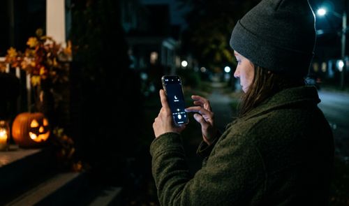 Persona ajustando la configuración de la cámara de su móvil para hacer una foto nocturna a una calabaza de Halloween iluminada.