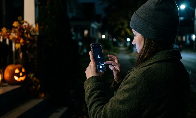 Persona ajustando la configuración de la cámara de su móvil para hacer una foto nocturna a una calabaza de Halloween iluminada.