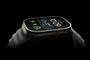 Vista lateral en ángulo de un Apple Watch con caja de titanio y correa deportiva sobre fondo negro.