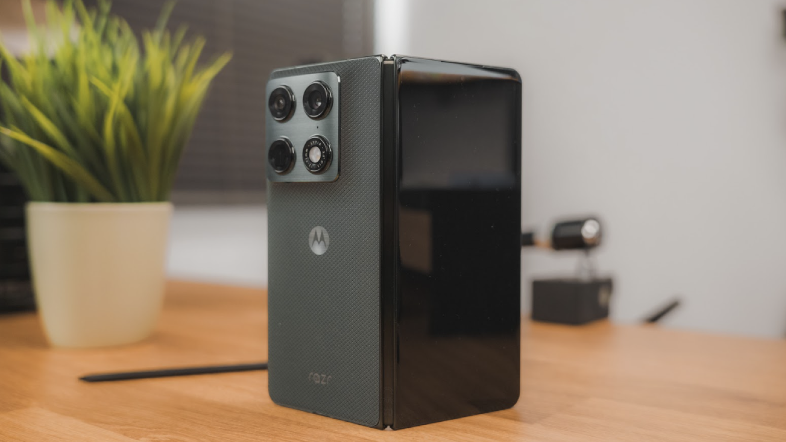 Teléfono plegable Motorola razr en posición vertical sobre una mesa, mostrando su sistema de cámaras traseras y el logotipo de la marca.
