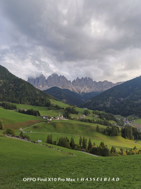 Paisaje de montaña con picos escarpados bajo un cielo nublado y valles de praderas verdes.
