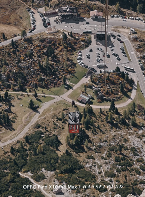 Vista aérea de un teleférico ascendiendo por una ladera de montaña hacia un aparcamiento y estación base.